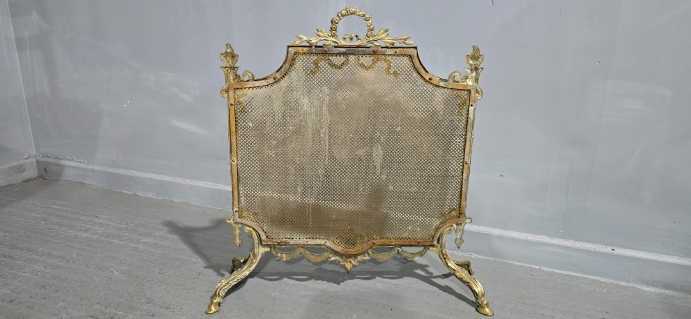 A Victorian gilt brass fire guard featuring a fine mesh panel, ribbon garlands, top wreath crest, and ornate torch finials. View IX