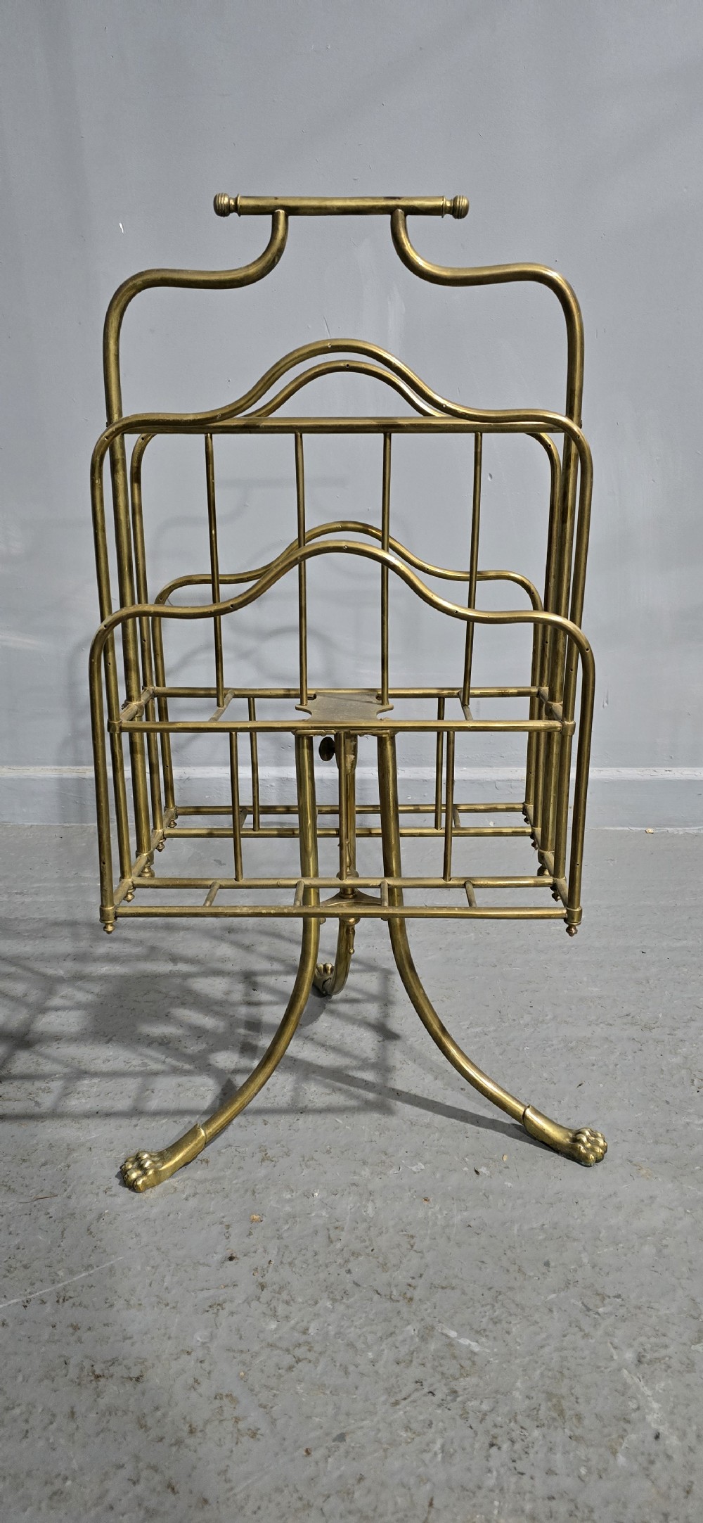 A Victorian brass revolving magazine stand featuring a wireframe rack with shaped dividers, supported on a tripod base with paw feet. View II