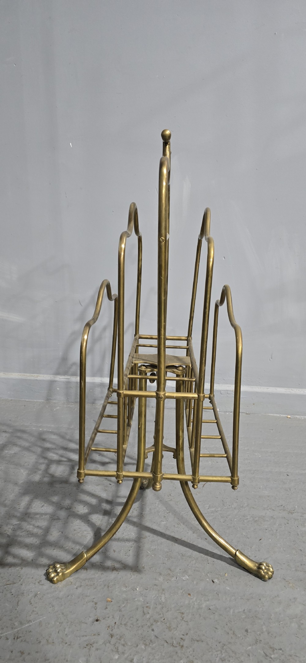 A Victorian brass revolving magazine stand featuring a wireframe rack with shaped dividers, supported on a tripod base with paw feet. View V