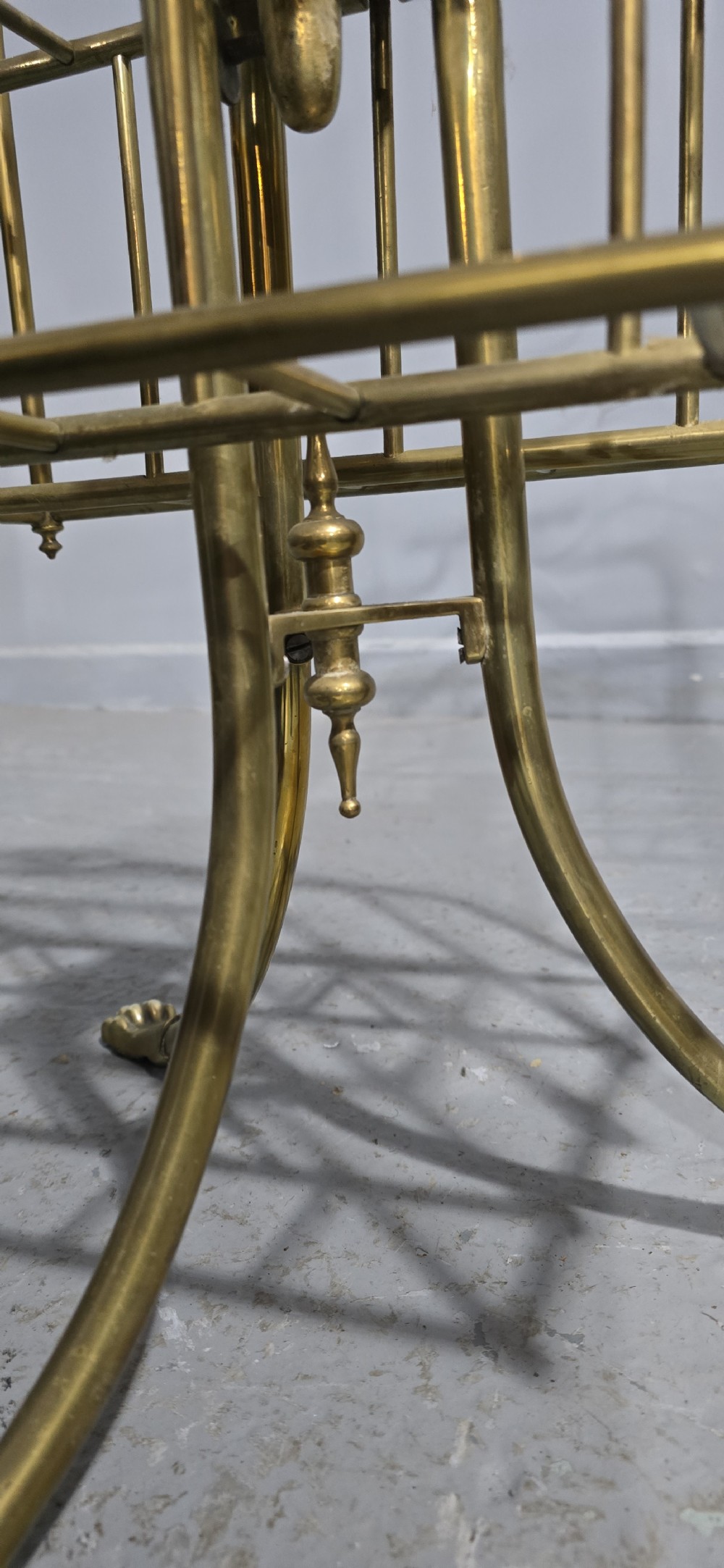 A Victorian brass revolving magazine stand featuring a wireframe rack with shaped dividers, supported on a tripod base with paw feet. View VI