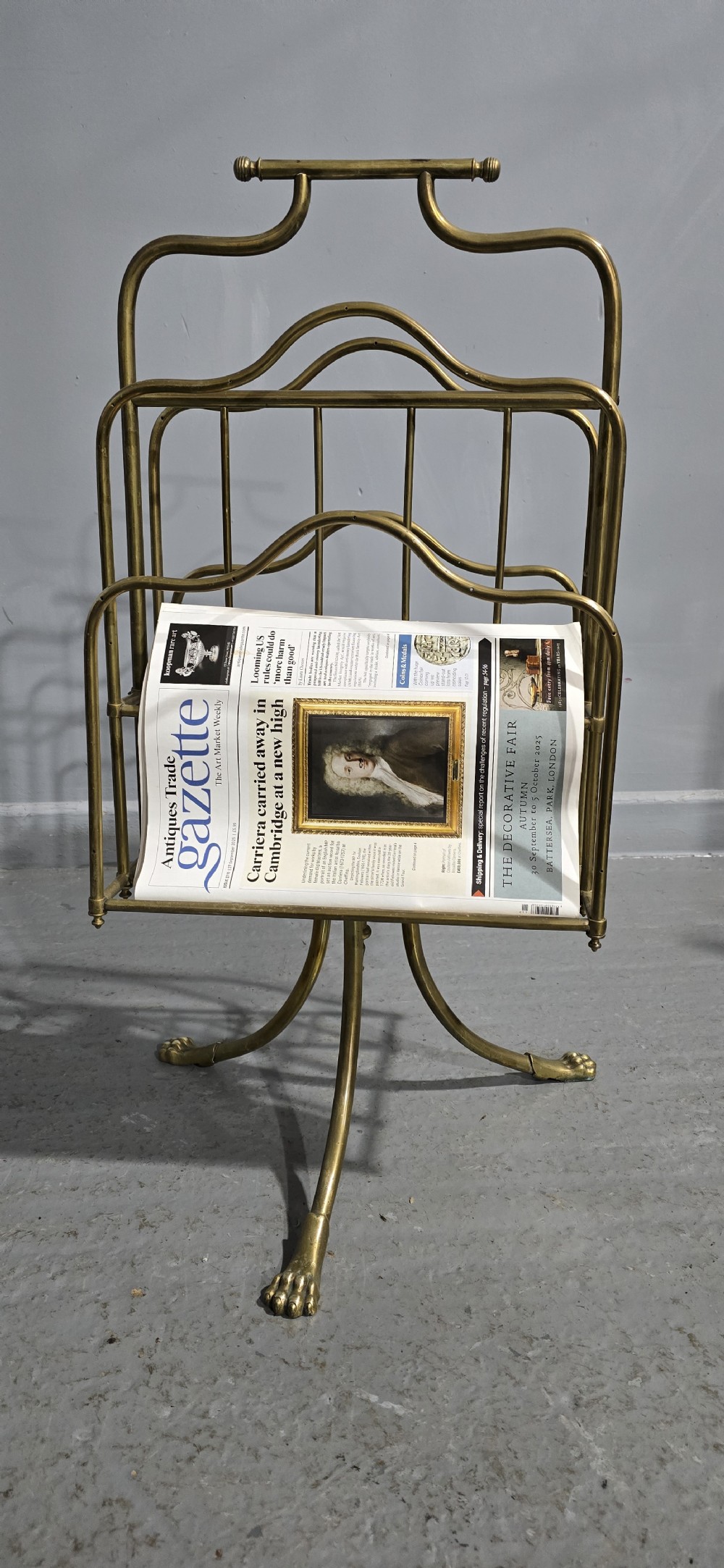 A Victorian brass revolving magazine stand featuring a wireframe rack with shaped dividers, supported on a tripod base with paw feet. View VIII