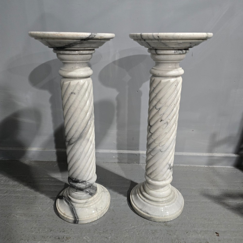 A pair of carved white and grey variegated marble pedestals with spiral shafts, circular capitals, and stepped moulded bases.