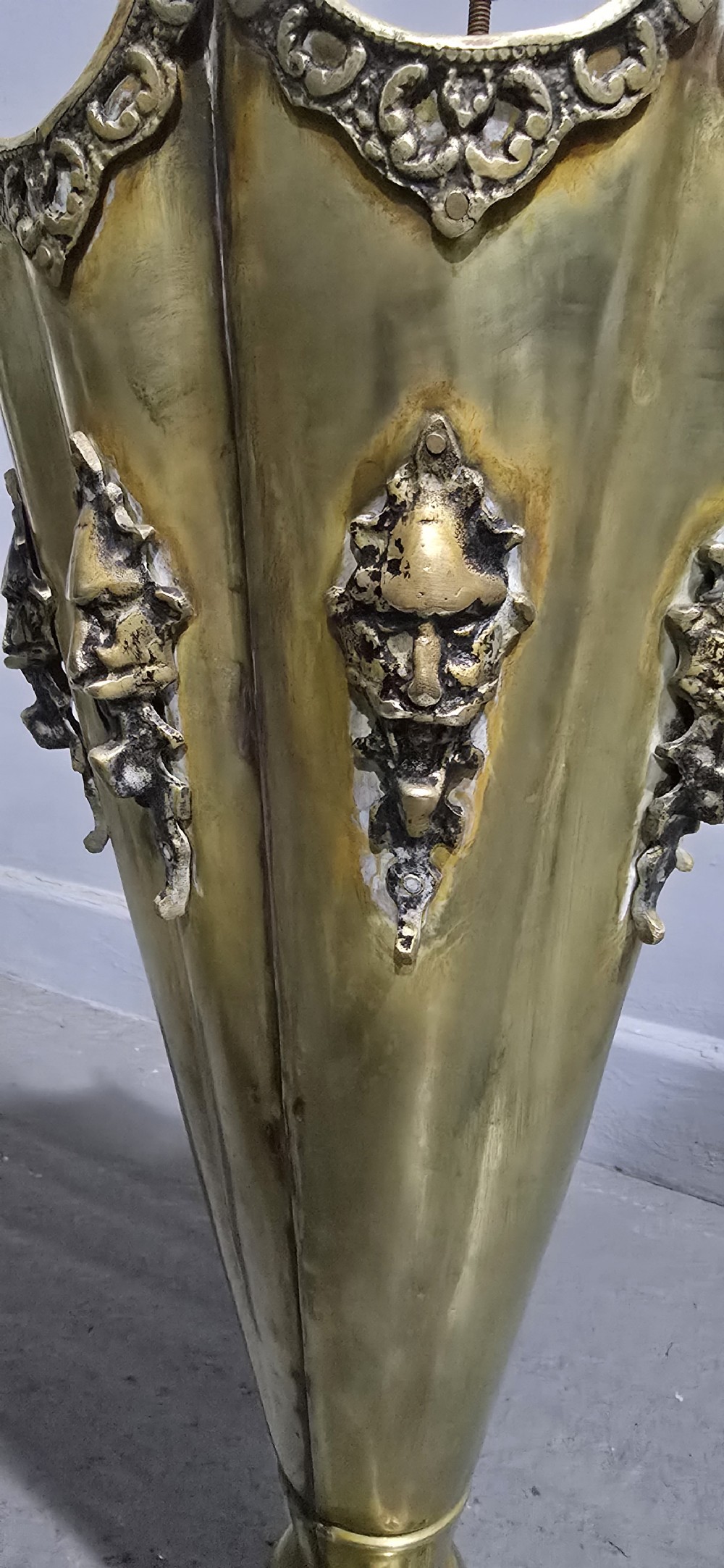 An antique umbrella-shaped brass umbrella stand featuring relief mascaron face details and a central curved hook handle. View VI