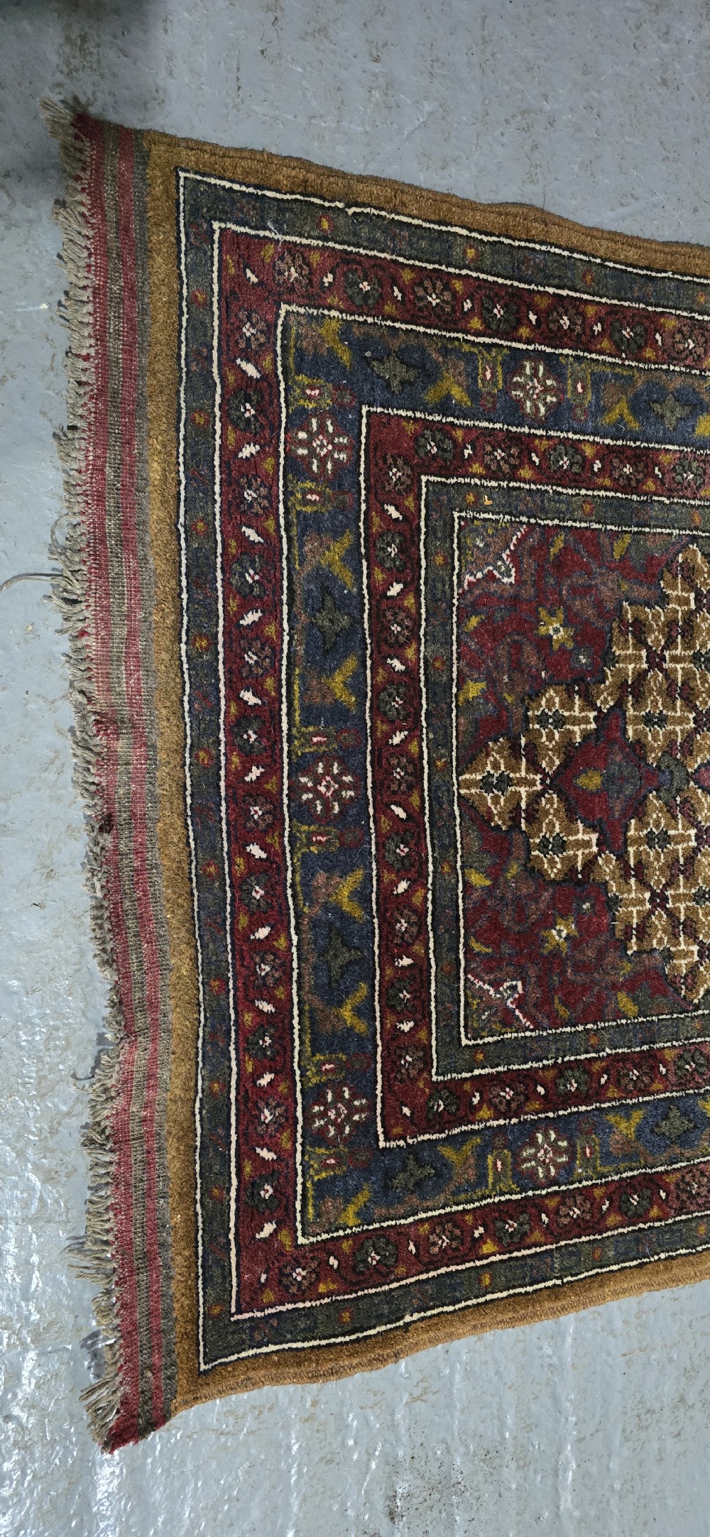 A long, narrow hand-knotted wool runner rug featuring repeating geometric medallions in deep red, navy blue, and ochre with intricate borders and fringed ends. View VII
