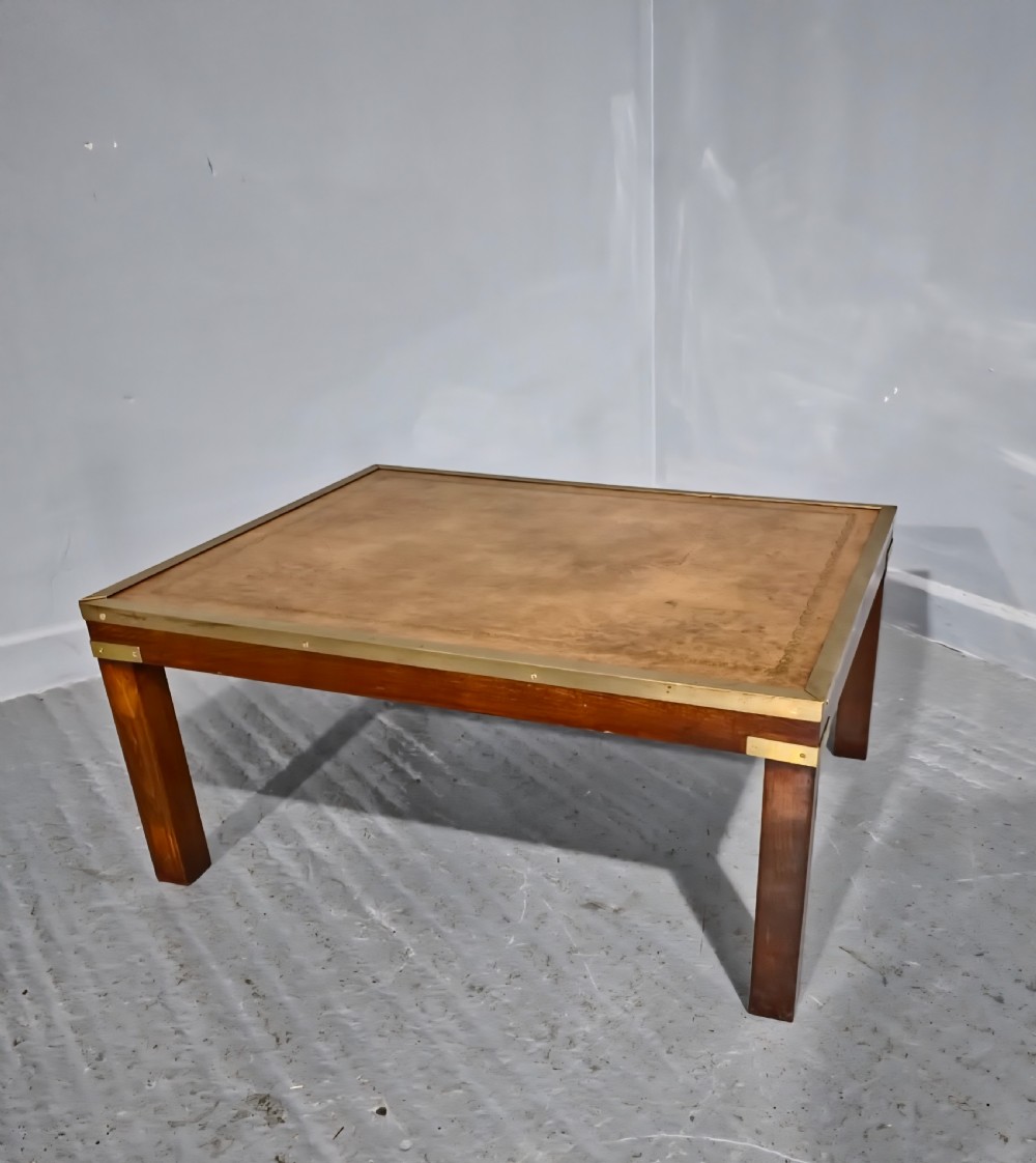A low rectangular mahogany coffee table featuring a leather inset top bordered by brass strapping and brass corner brackets.