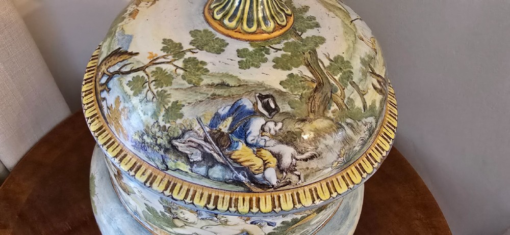 An 18th-century Italian tin-glazed earthenware lidded jar decorated with painted classical landscapes, cherubs, and architectural ruins. View X