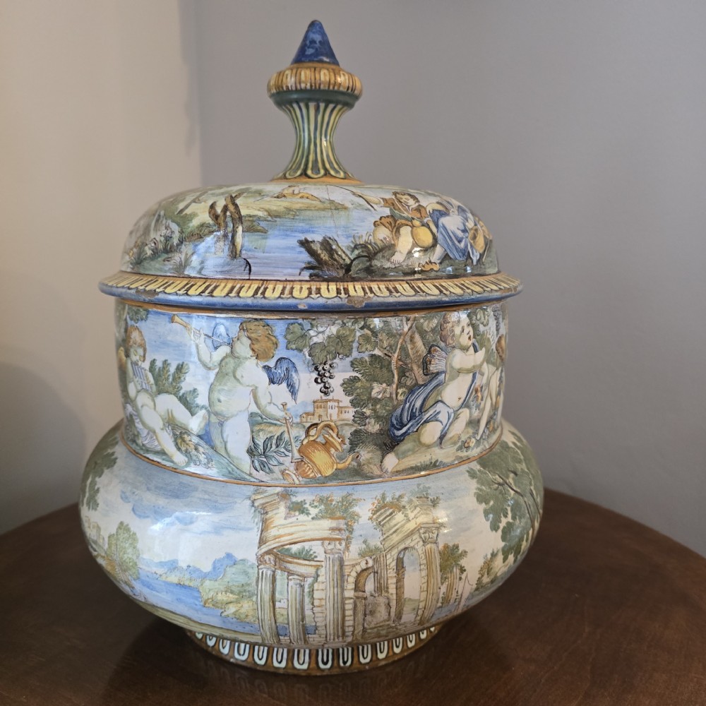 An 18th-century Italian tin-glazed earthenware lidded jar decorated with painted classical landscapes, cherubs, and architectural ruins.