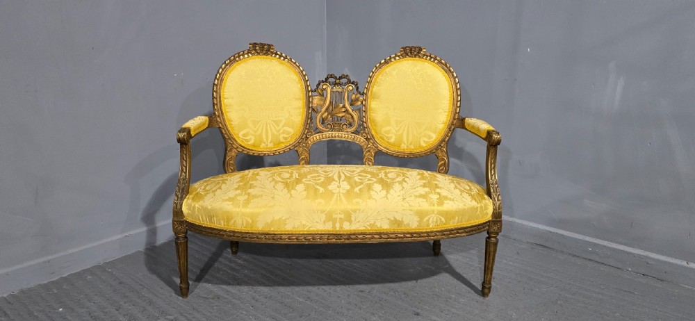 An antique French Louis XVI style giltwood two-seat sofa with twin oval medallion backrests, a central carved lyre motif, fluted legs, and yellow silk damask upholstery. View II