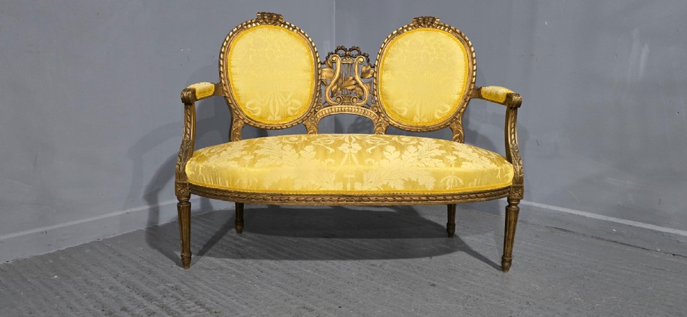 An antique French Louis XVI style giltwood two-seat sofa with twin oval medallion backrests, a central carved lyre motif, fluted legs, and yellow silk damask upholstery. View III