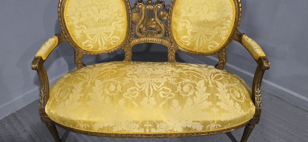 An antique French Louis XVI style giltwood two-seat sofa with twin oval medallion backrests, a central carved lyre motif, fluted legs, and yellow silk damask upholstery. View IV