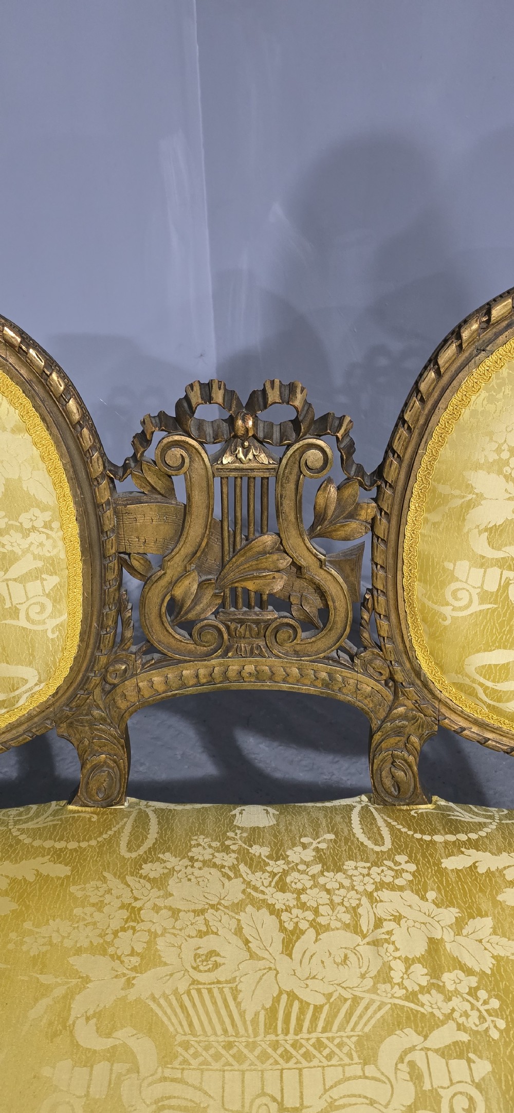 An antique French Louis XVI style giltwood two-seat sofa with twin oval medallion backrests, a central carved lyre motif, fluted legs, and yellow silk damask upholstery. View VII