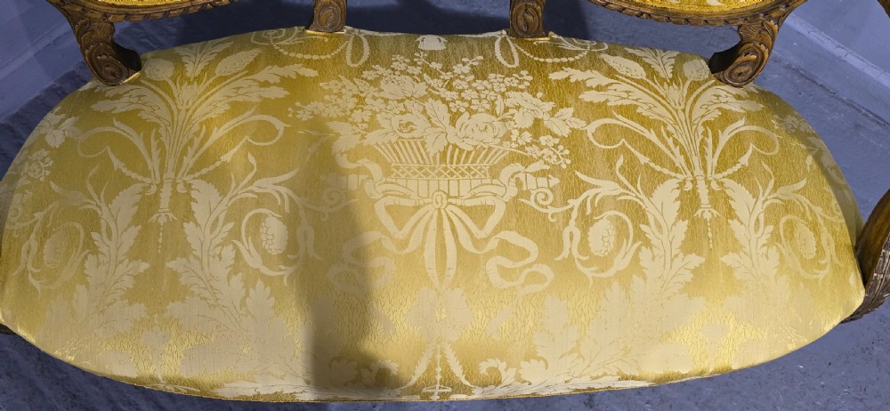 An antique French Louis XVI style giltwood two-seat sofa with twin oval medallion backrests, a central carved lyre motif, fluted legs, and yellow silk damask upholstery. View VIII