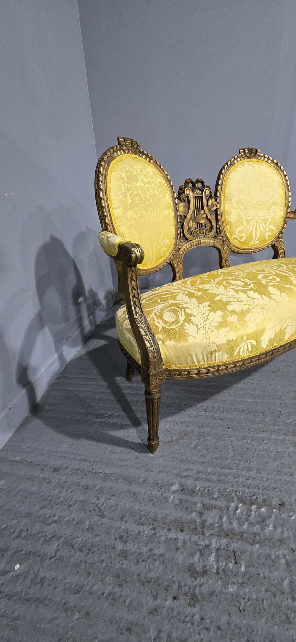 An antique French Louis XVI style giltwood two-seat sofa with twin oval medallion backrests, a central carved lyre motif, fluted legs, and yellow silk damask upholstery. View XII