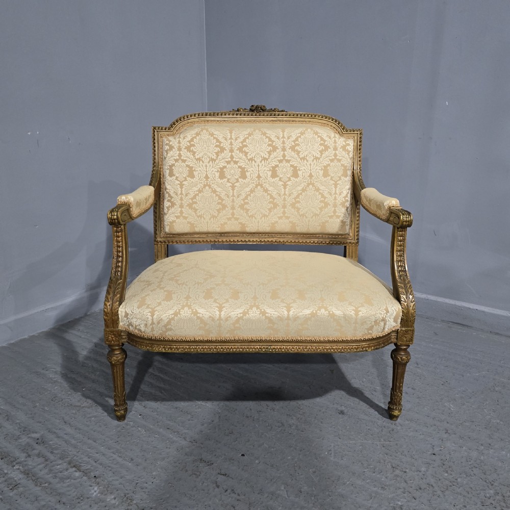 A French Louis XVI style two-seat settee featuring a carved giltwood frame with fluted legs and cream floral damask upholstery.