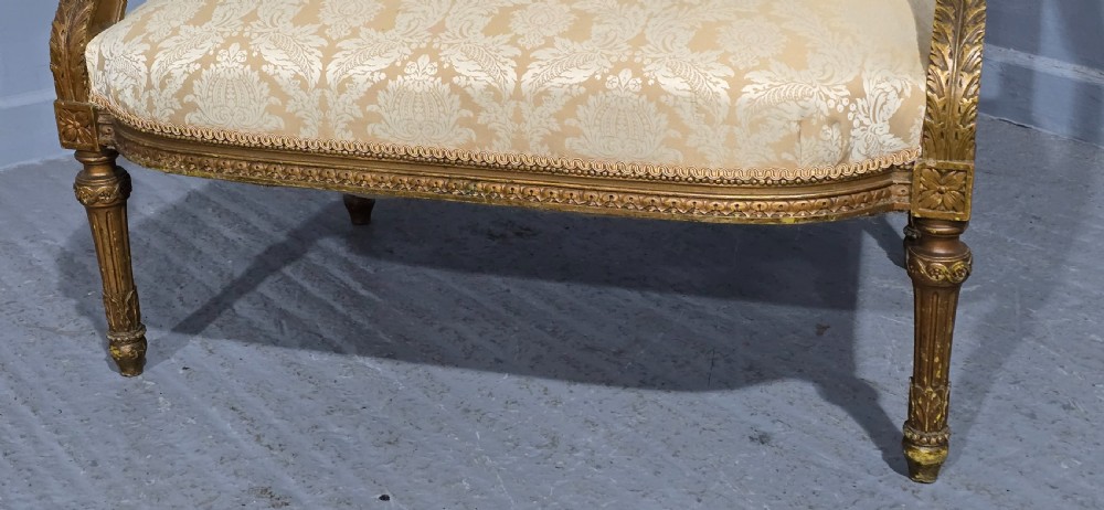 A French Louis XVI style two-seat settee featuring a carved giltwood frame with fluted legs and cream floral damask upholstery. View VI
