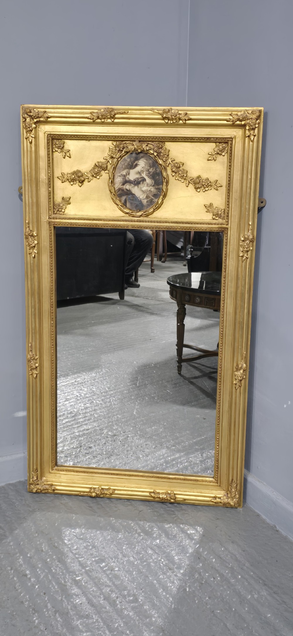 An antique French giltwood trumeau mirror featuring a tall rectangular frame topped with a carved oval painted portrait inset and floral garlands. View II