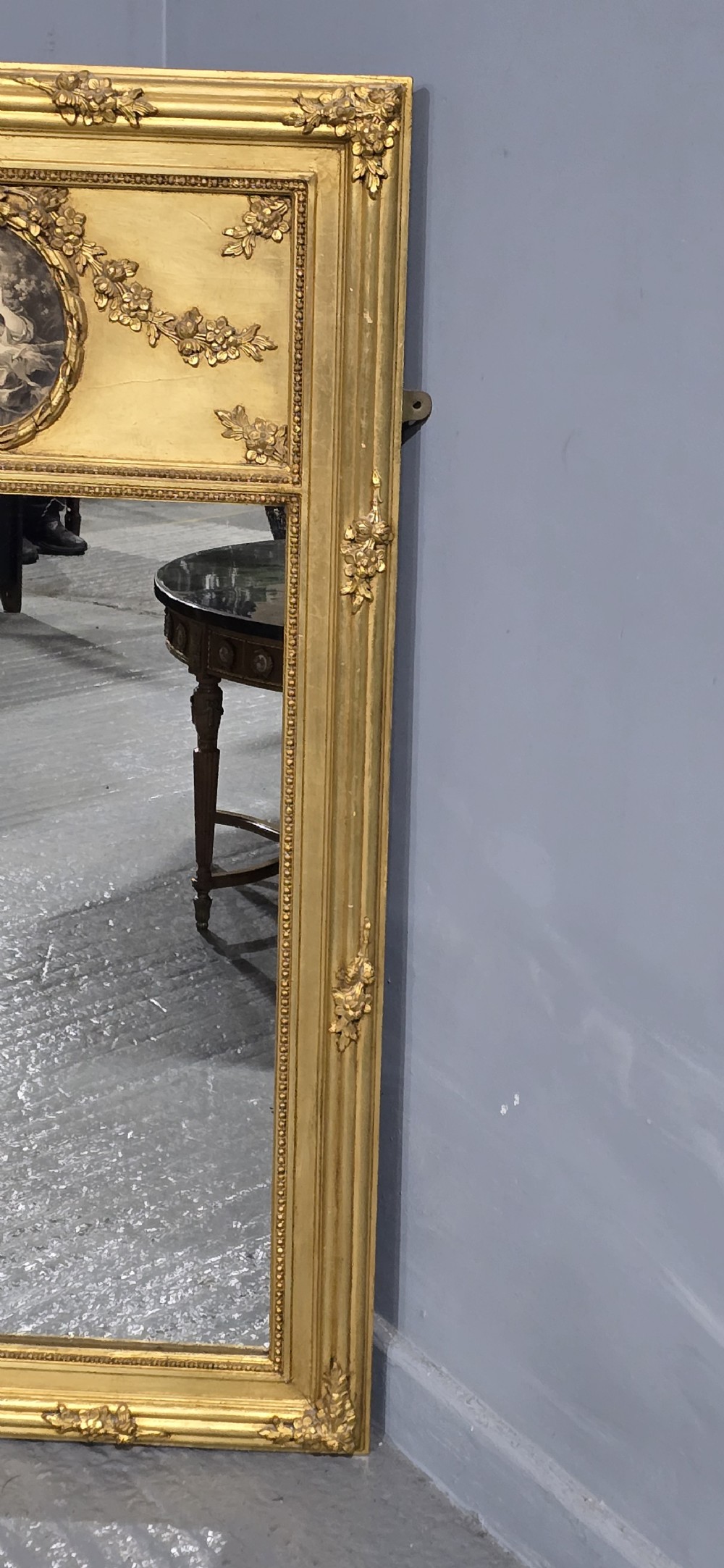 An antique French giltwood trumeau mirror featuring a tall rectangular frame topped with a carved oval painted portrait inset and floral garlands. View V