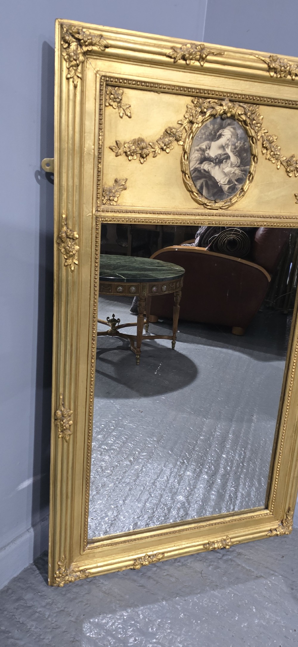 An antique French giltwood trumeau mirror featuring a tall rectangular frame topped with a carved oval painted portrait inset and floral garlands. View VI