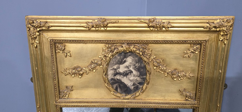 An antique French giltwood trumeau mirror featuring a tall rectangular frame topped with a carved oval painted portrait inset and floral garlands. View VII