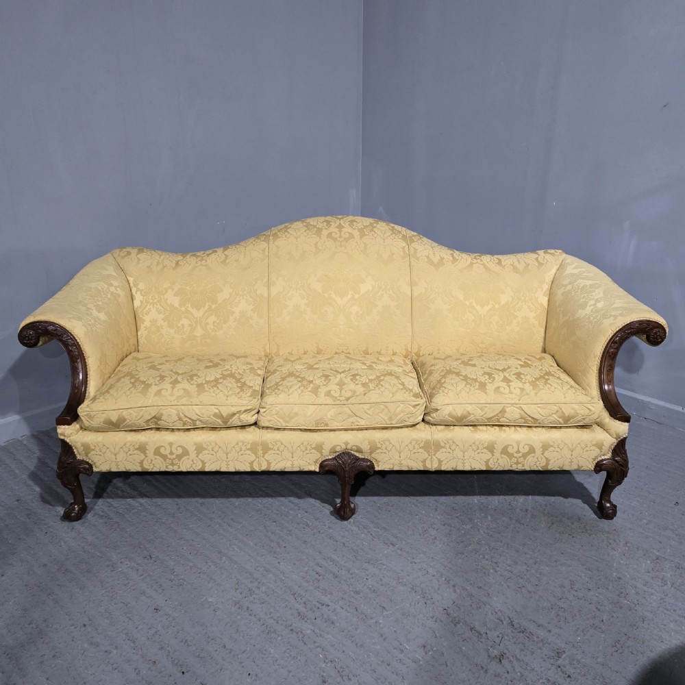 A camelback sofa upholstered in patterned yellow damask fabric with carved mahogany scroll arms and cabriole legs terminating in ball and claw feet.