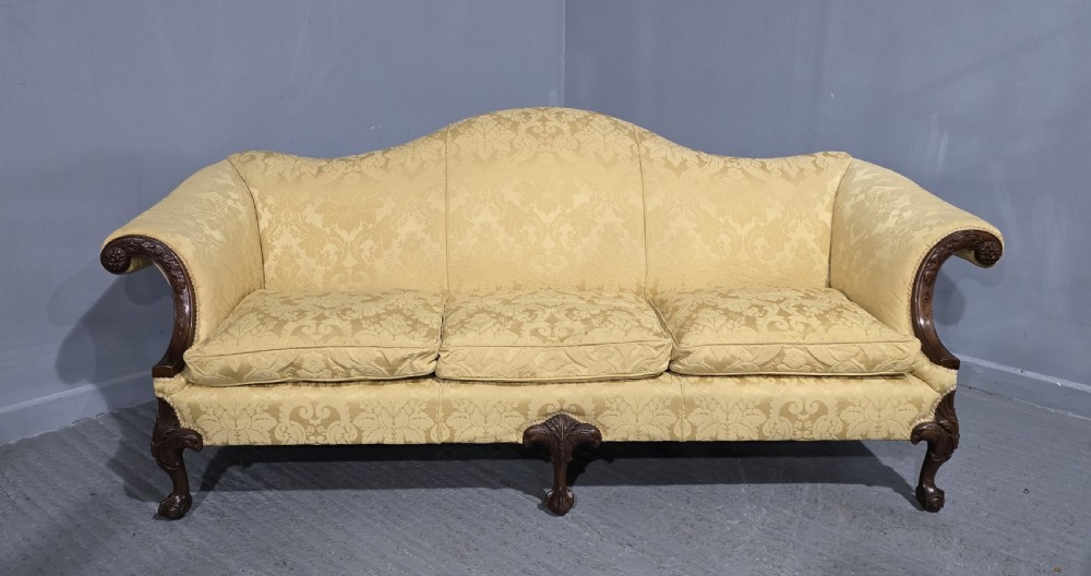 A camelback sofa upholstered in patterned yellow damask fabric with carved mahogany scroll arms and cabriole legs terminating in ball and claw feet. View II