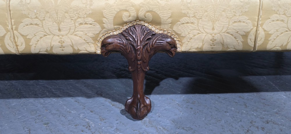 A camelback sofa upholstered in patterned yellow damask fabric with carved mahogany scroll arms and cabriole legs terminating in ball and claw feet. View III