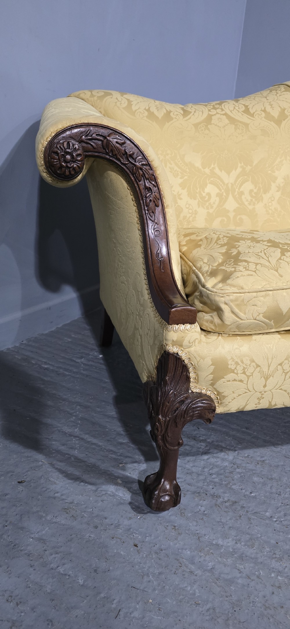 A camelback sofa upholstered in patterned yellow damask fabric with carved mahogany scroll arms and cabriole legs terminating in ball and claw feet. View IV