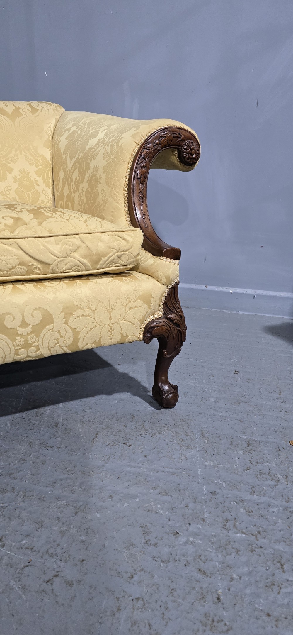 A camelback sofa upholstered in patterned yellow damask fabric with carved mahogany scroll arms and cabriole legs terminating in ball and claw feet. View V