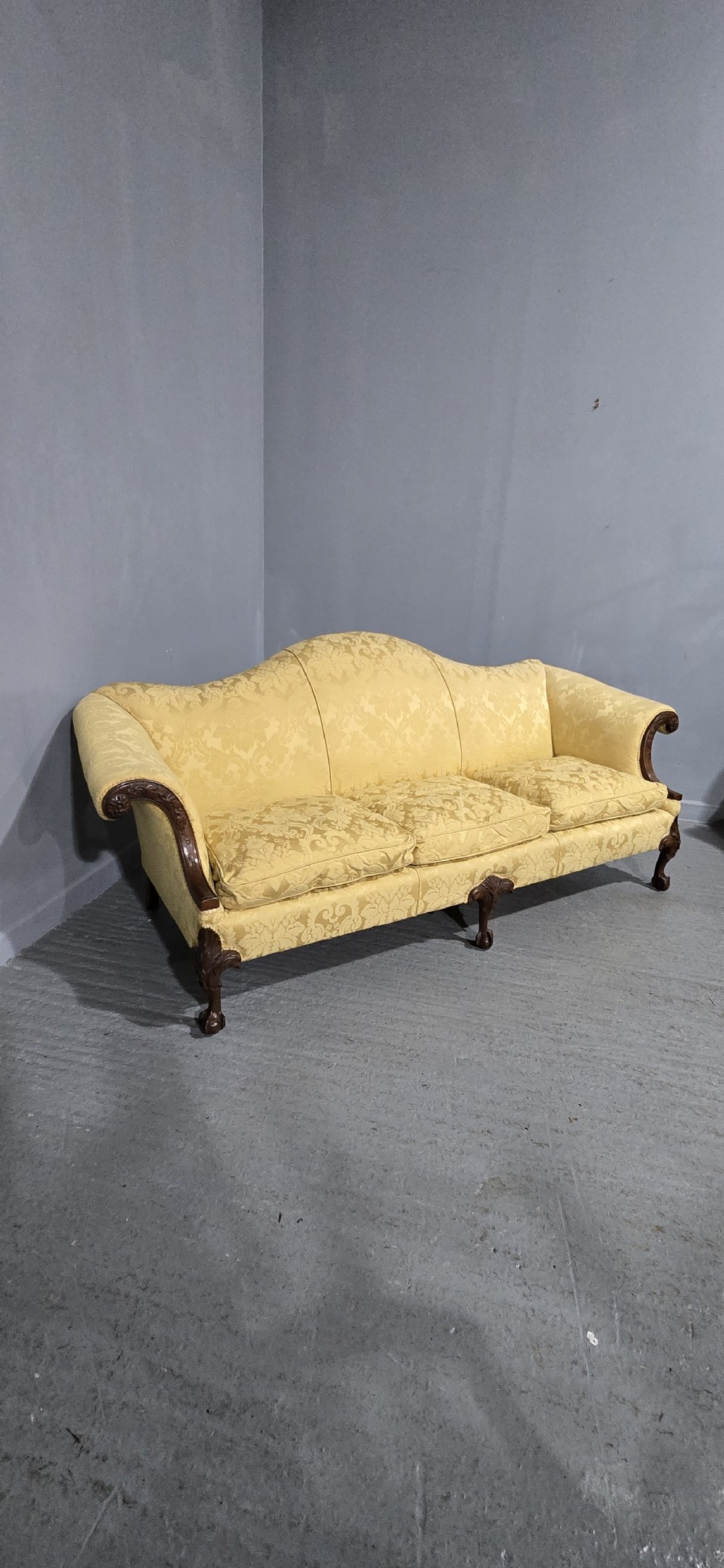 A camelback sofa upholstered in patterned yellow damask fabric with carved mahogany scroll arms and cabriole legs terminating in ball and claw feet. View X