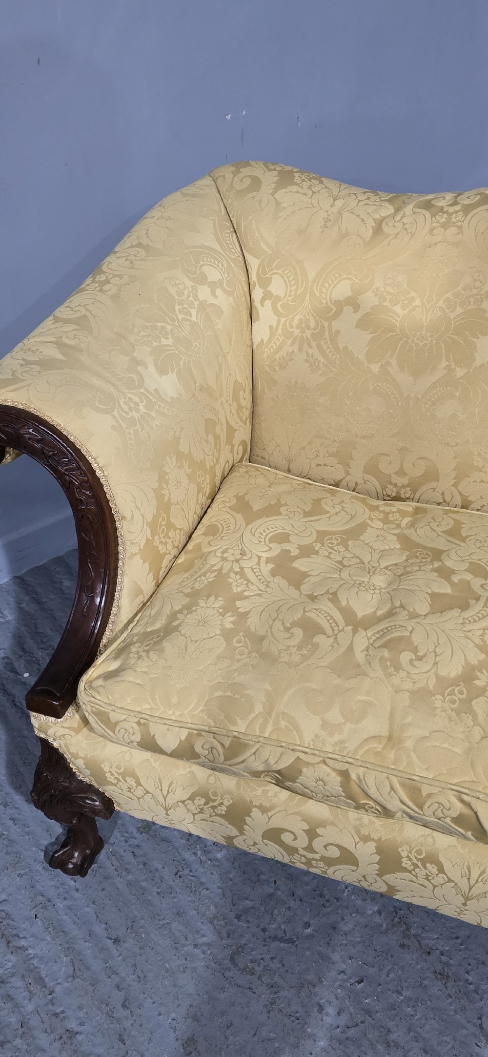 A camelback sofa upholstered in patterned yellow damask fabric with carved mahogany scroll arms and cabriole legs terminating in ball and claw feet. View XV