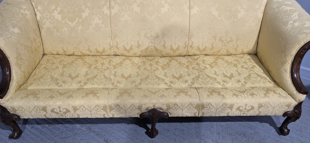 A camelback sofa upholstered in patterned yellow damask fabric with carved mahogany scroll arms and cabriole legs terminating in ball and claw feet. View XVII