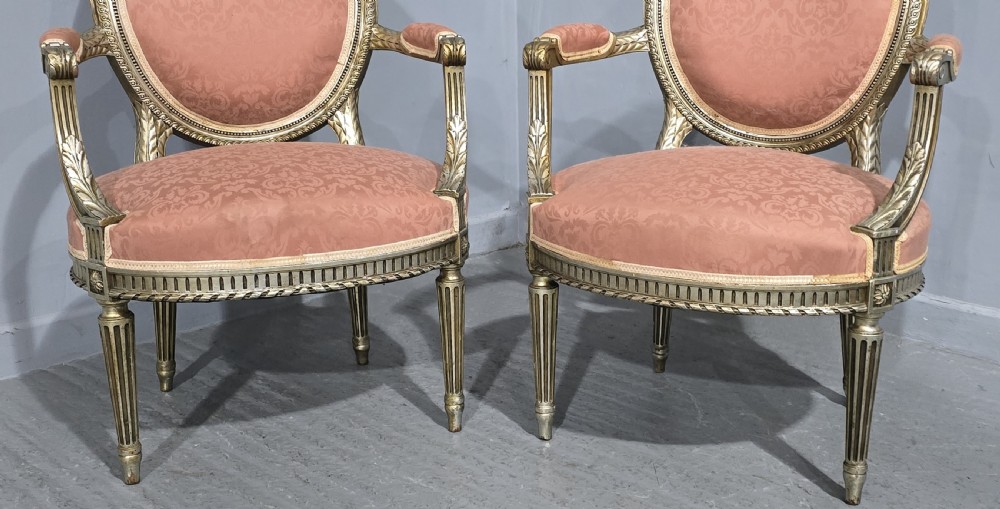 A pair of French Louis XVI style elbow chairs featuring silver gilt carved frames with oval backs, fluted legs, and pink patterned upholstery. View II