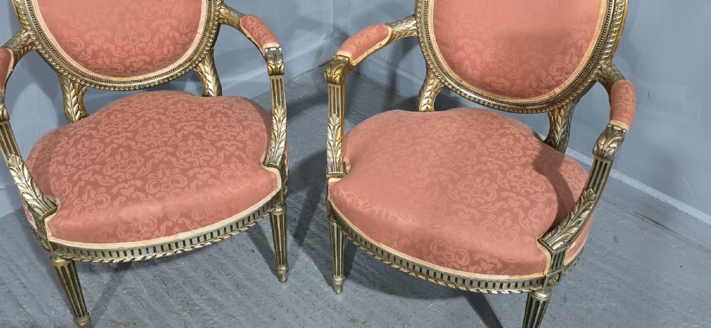 A pair of French Louis XVI style elbow chairs featuring silver gilt carved frames with oval backs, fluted legs, and pink patterned upholstery. View V