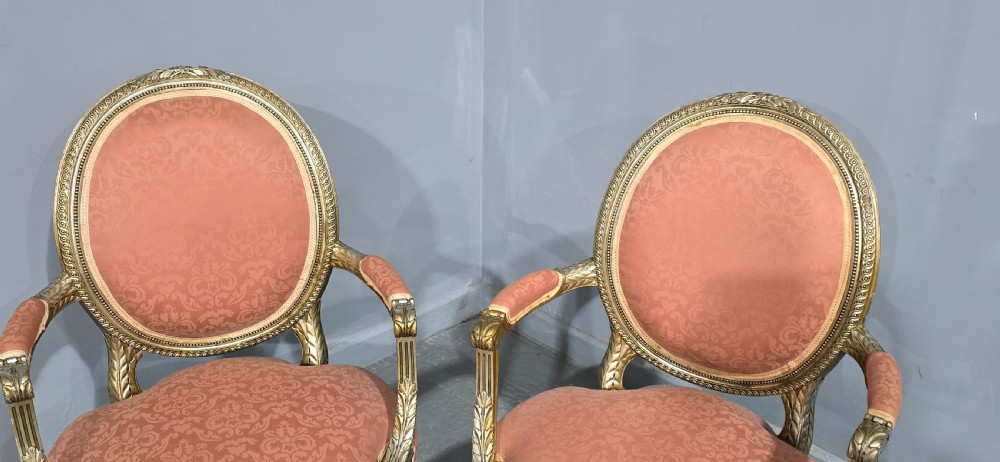 A pair of French Louis XVI style elbow chairs featuring silver gilt carved frames with oval backs, fluted legs, and pink patterned upholstery. View VI