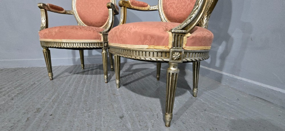 A pair of French Louis XVI style elbow chairs featuring silver gilt carved frames with oval backs, fluted legs, and pink patterned upholstery. View IX