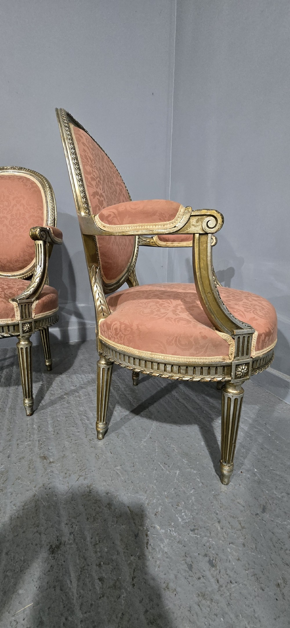 A pair of French Louis XVI style elbow chairs featuring silver gilt carved frames with oval backs, fluted legs, and pink patterned upholstery. View XI