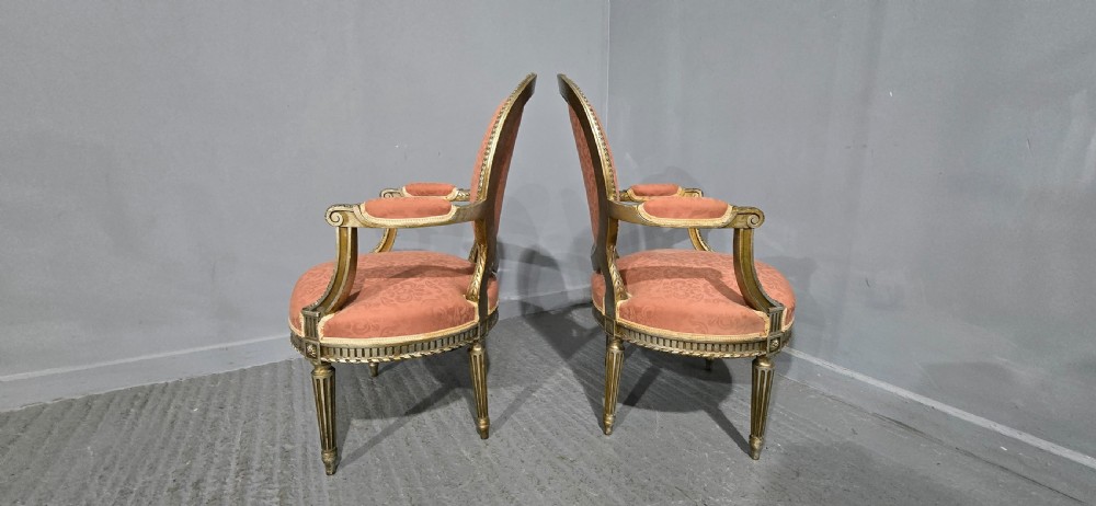 A pair of French Louis XVI style elbow chairs featuring silver gilt carved frames with oval backs, fluted legs, and pink patterned upholstery. View XII