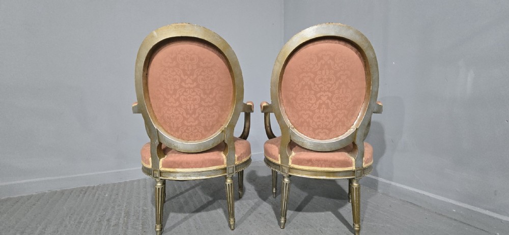 A pair of French Louis XVI style elbow chairs featuring silver gilt carved frames with oval backs, fluted legs, and pink patterned upholstery. View XIII