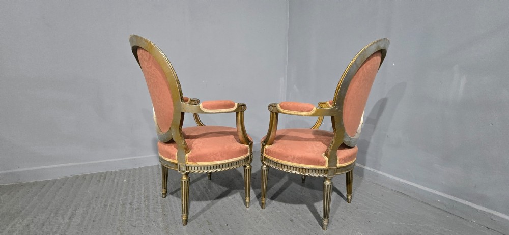 A pair of French Louis XVI style elbow chairs featuring silver gilt carved frames with oval backs, fluted legs, and pink patterned upholstery. View XIV