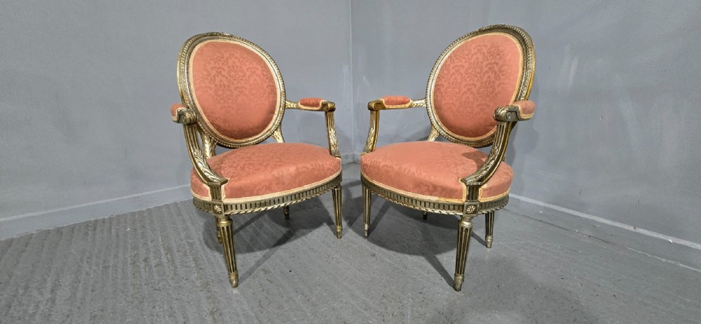 A pair of French Louis XVI style elbow chairs featuring silver gilt carved frames with oval backs, fluted legs, and pink patterned upholstery. View XV