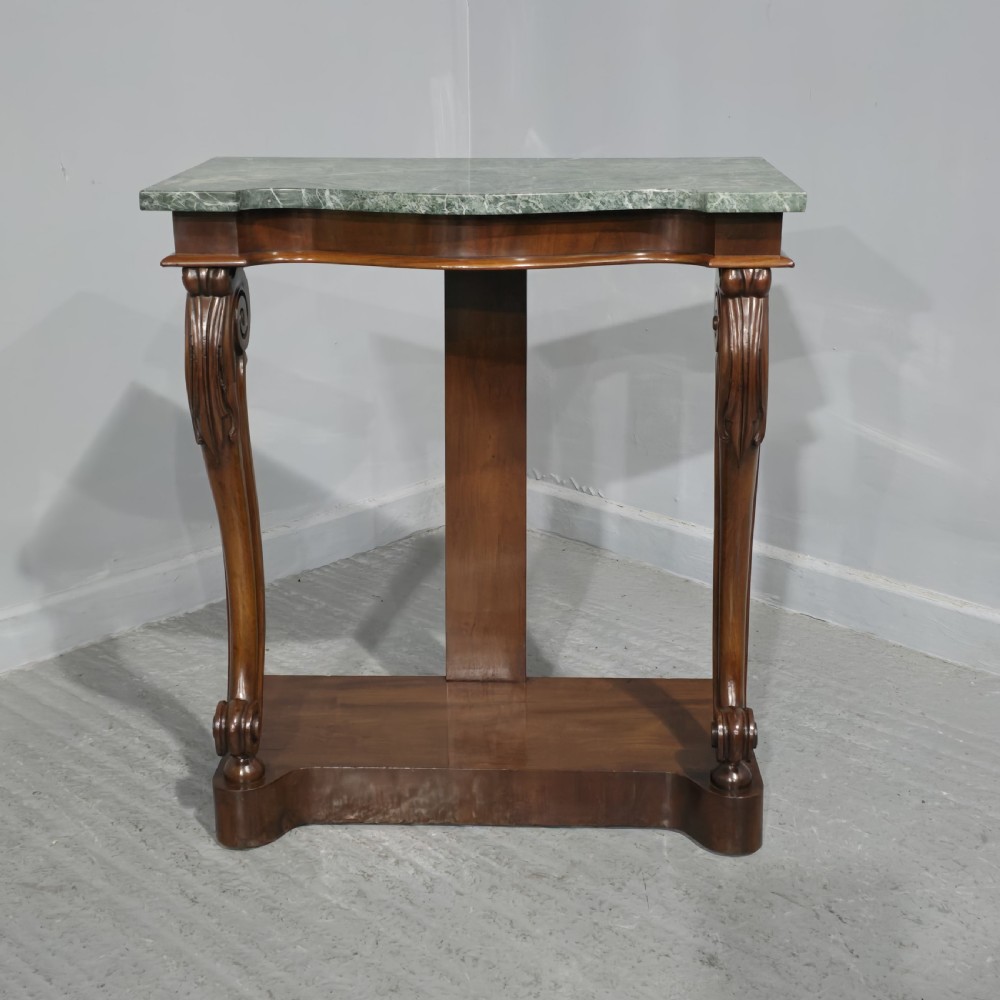 A mahogany console table featuring a green marble top supported by carved scrolled front legs on a plinth base.