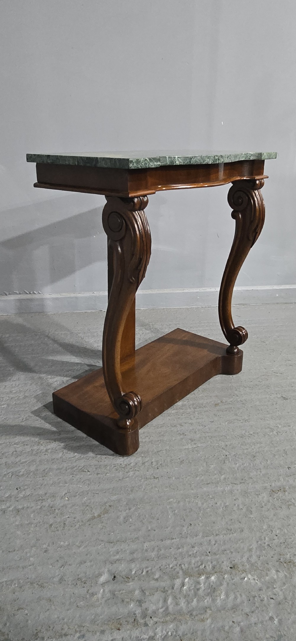 A mahogany console table featuring a green marble top supported by carved scrolled front legs on a plinth base. View III