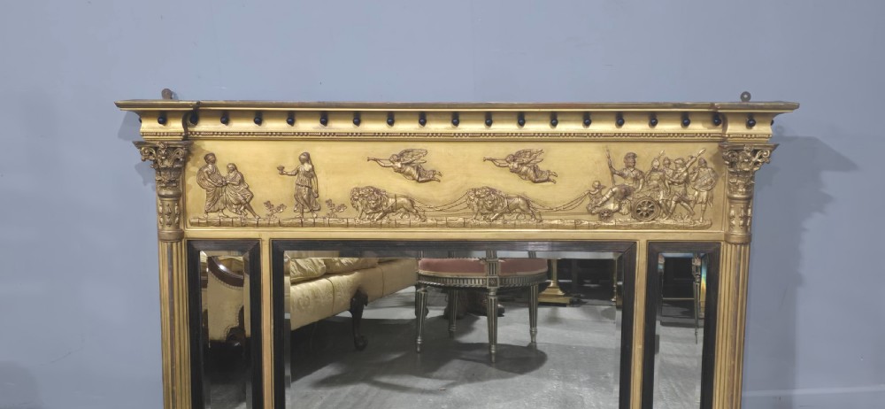 A wide Regency giltwood triple-plate overmantel mirror featuring a classical relief frieze depicting figures and chariot above fluted columns. View II