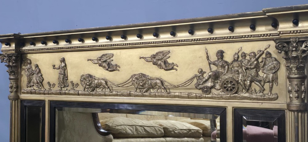 A wide Regency giltwood triple-plate overmantel mirror featuring a classical relief frieze depicting figures and chariot above fluted columns. View V