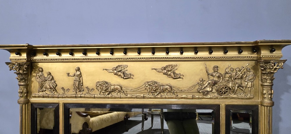 A wide Regency giltwood triple-plate overmantel mirror featuring a classical relief frieze depicting figures and chariot above fluted columns. View IX
