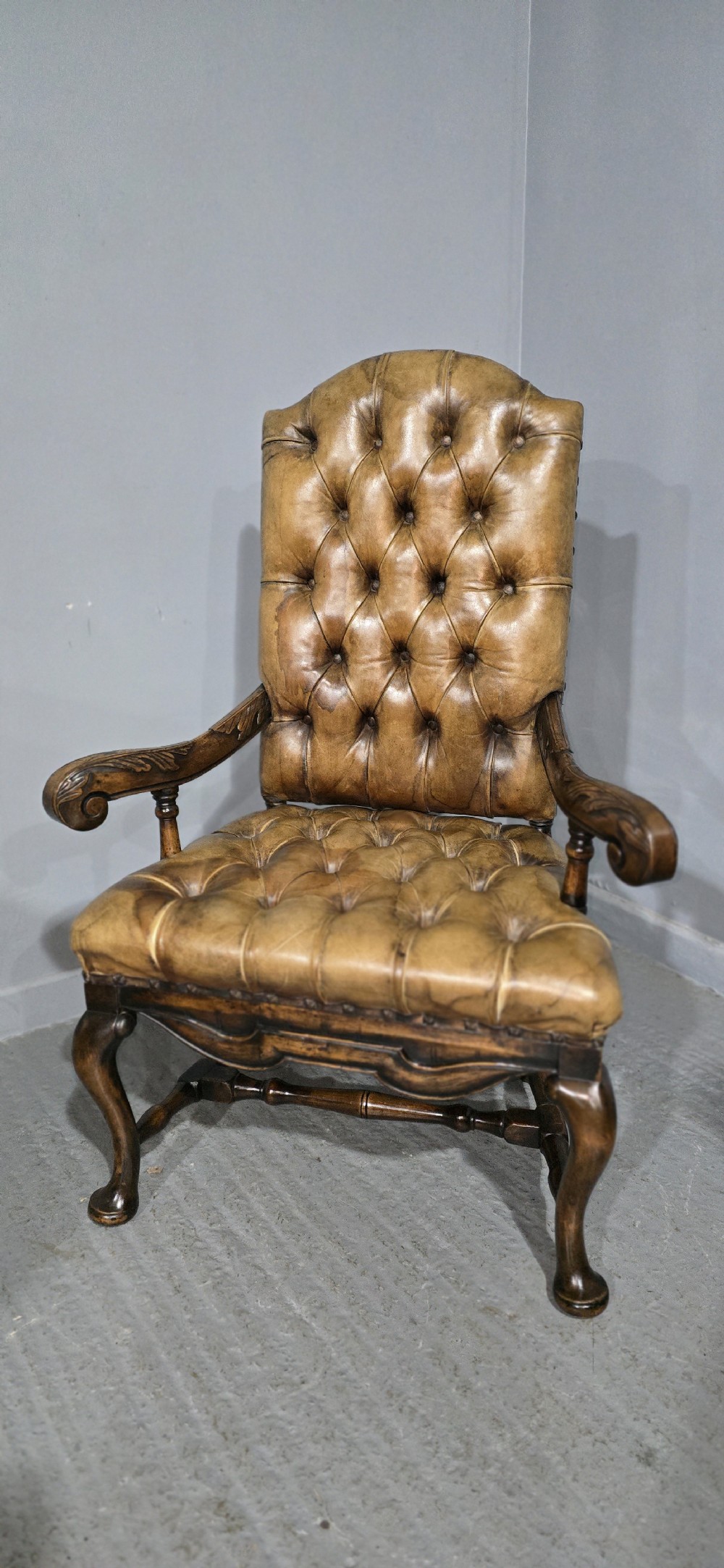 An antique William and Mary style high-back armchair upholstered in deep-buttoned tan leather with carved walnut arms and legs. View II