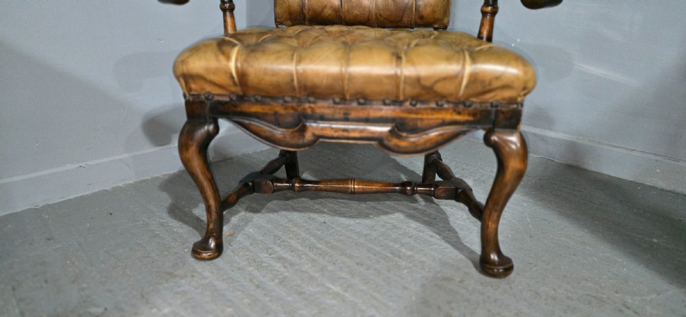 An antique William and Mary style high-back armchair upholstered in deep-buttoned tan leather with carved walnut arms and legs. View III