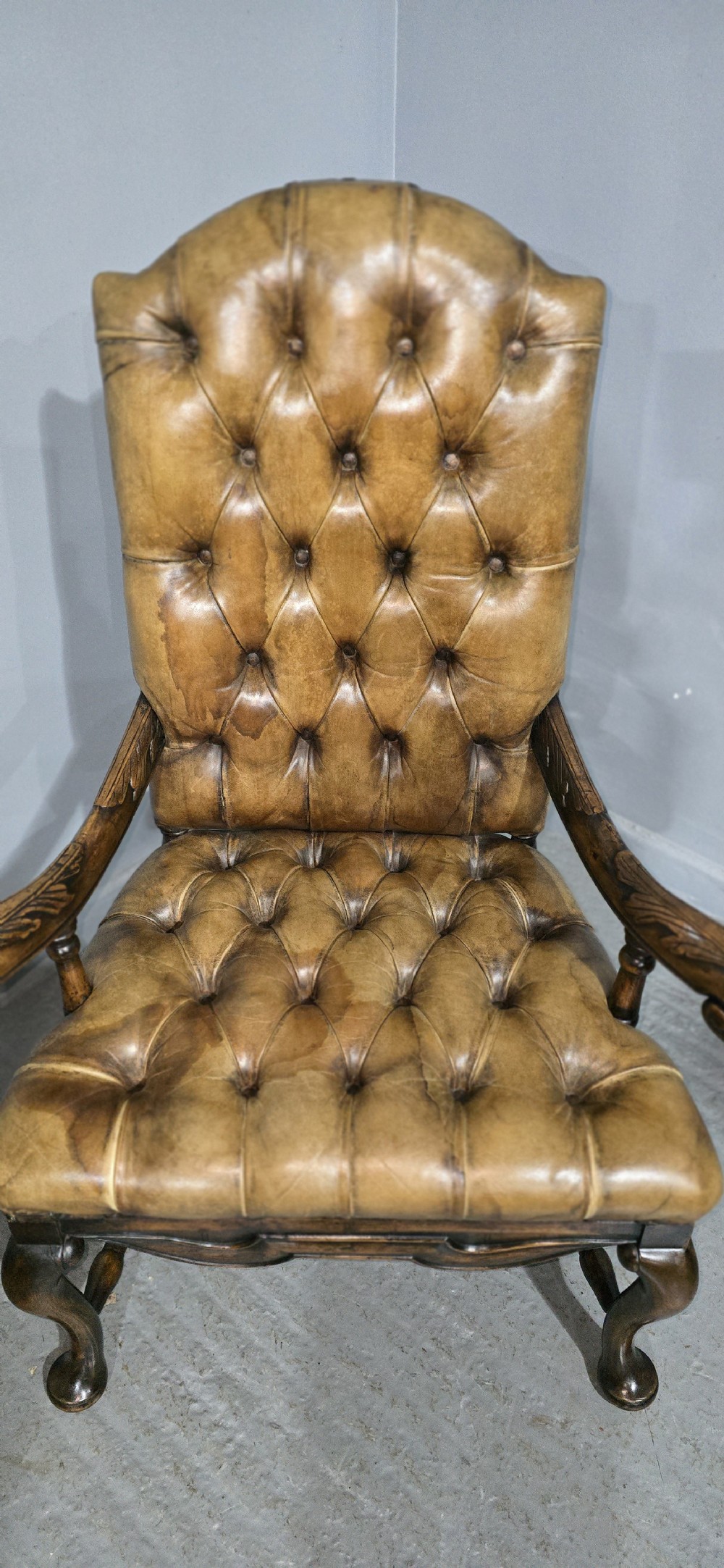 An antique William and Mary style high-back armchair upholstered in deep-buttoned tan leather with carved walnut arms and legs. View V