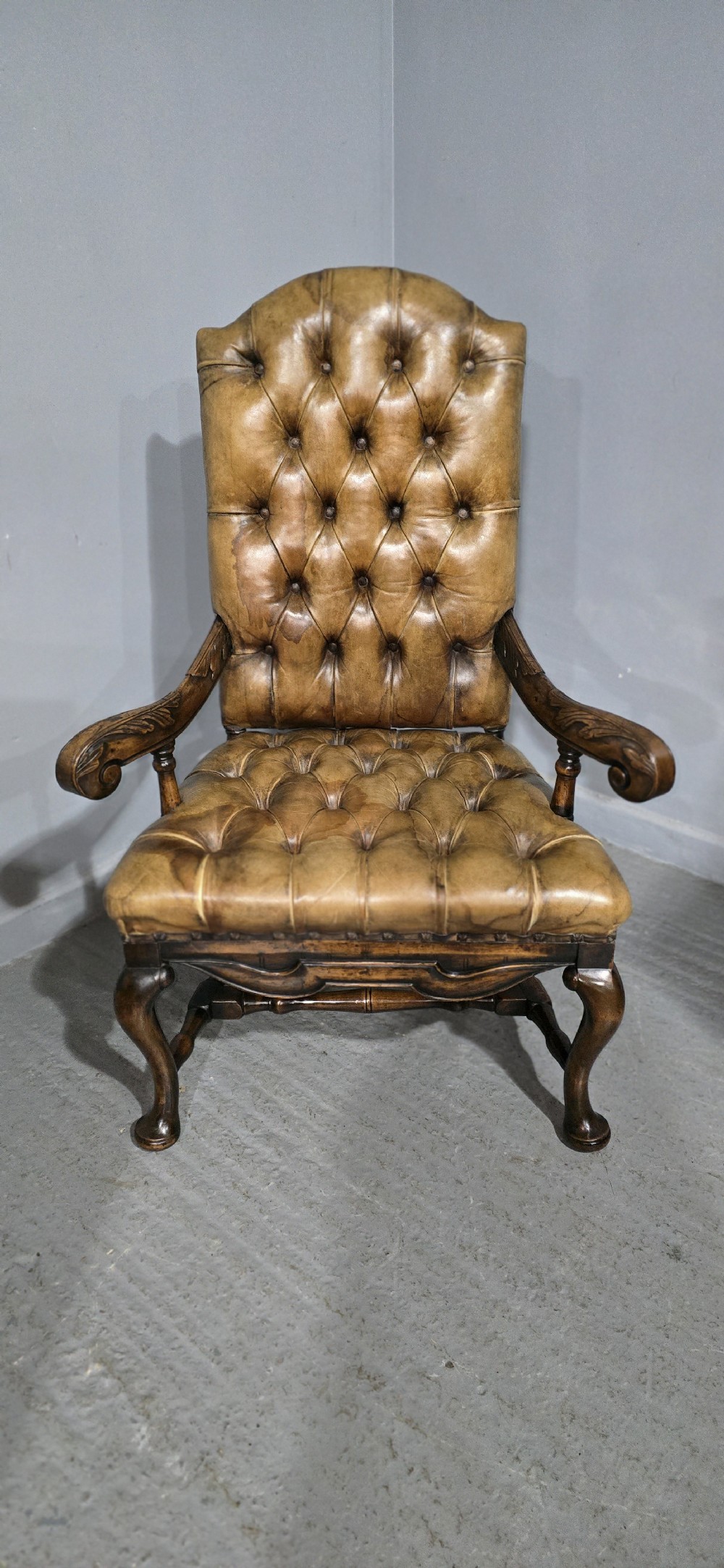 An antique William and Mary style high-back armchair upholstered in deep-buttoned tan leather with carved walnut arms and legs. View VI