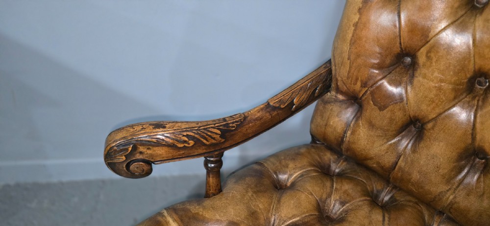 An antique William and Mary style high-back armchair upholstered in deep-buttoned tan leather with carved walnut arms and legs. View VII